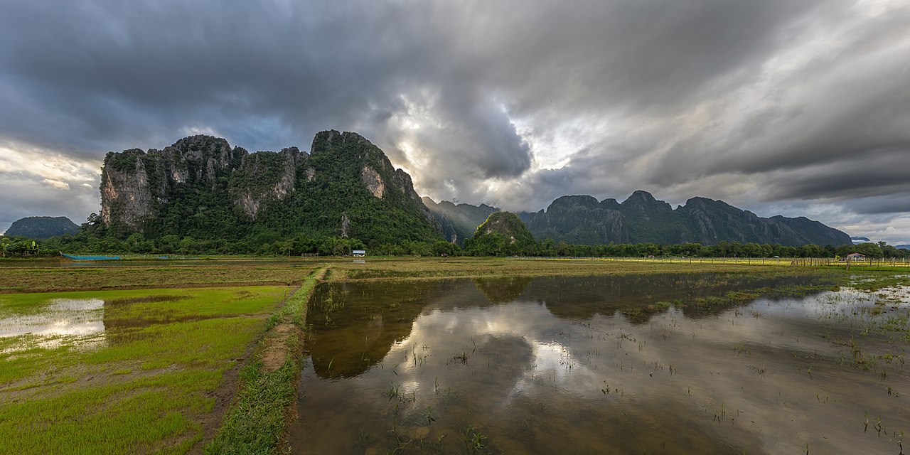 1280px-Panoramic_of_water_reflection_of_the_mountains_of_Vang_Vieng_with_cloudy_sky_in_paddy_fields.jpeg