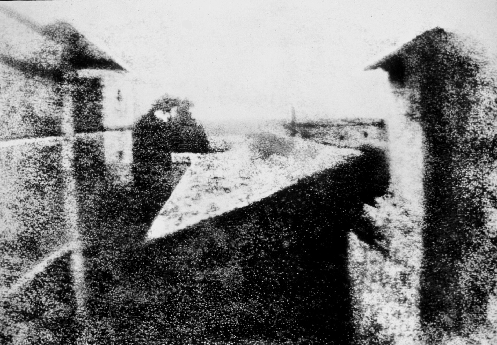 Imagen en blanco y negro, granulada y contrastada, de tejados y edificios vistos desde una ventana, con un edificio alto a la izquierda y otro a la derecha