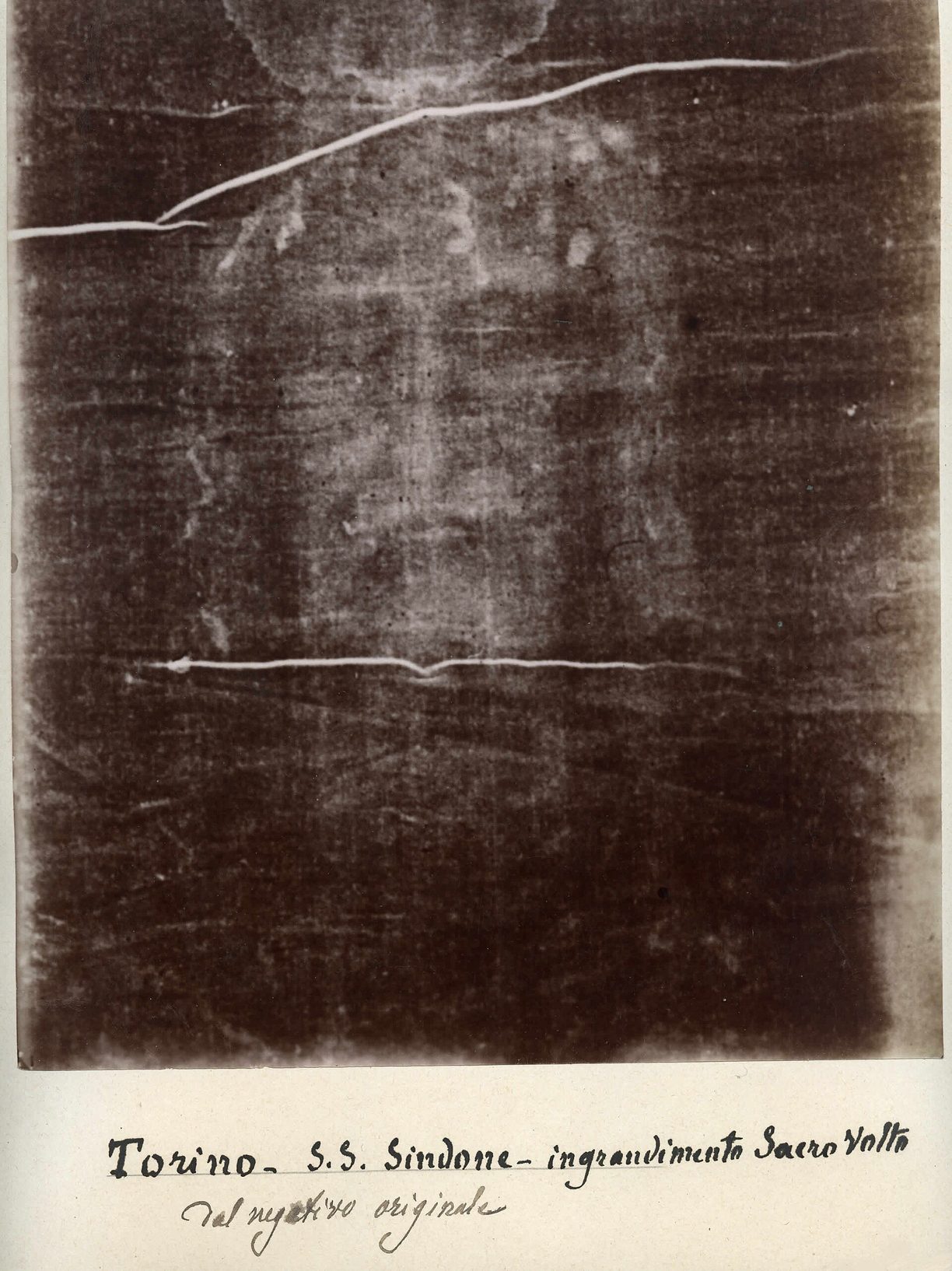 Fotografía antigua en tonos sepia oscuros con un rostro masculino barbado que aparece en claro sobre fondo oscuro, con una anotación manuscrita al pie