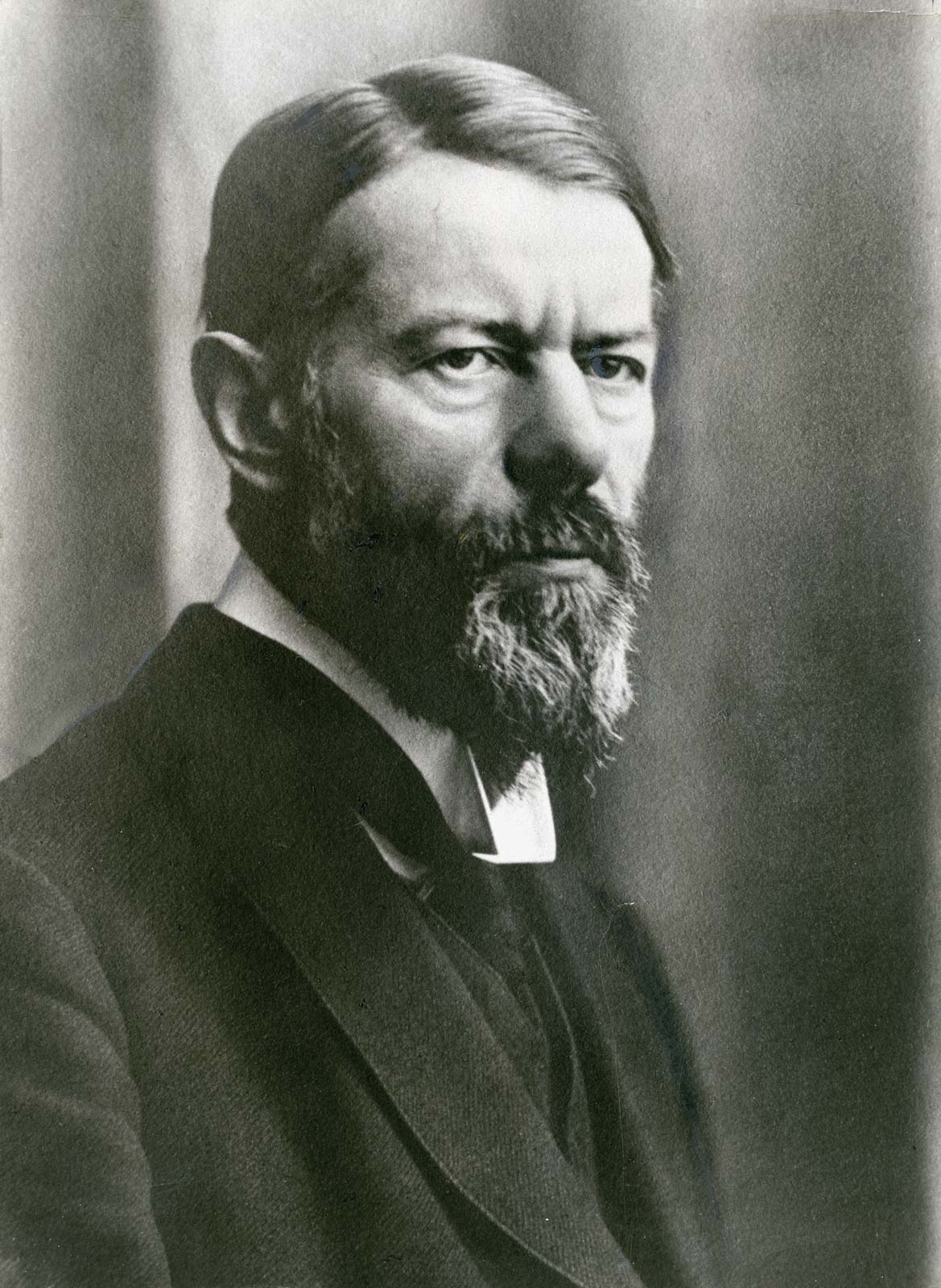 Retrato fotográfico en blanco y negro de un hombre barbado de mirada seria, con traje oscuro